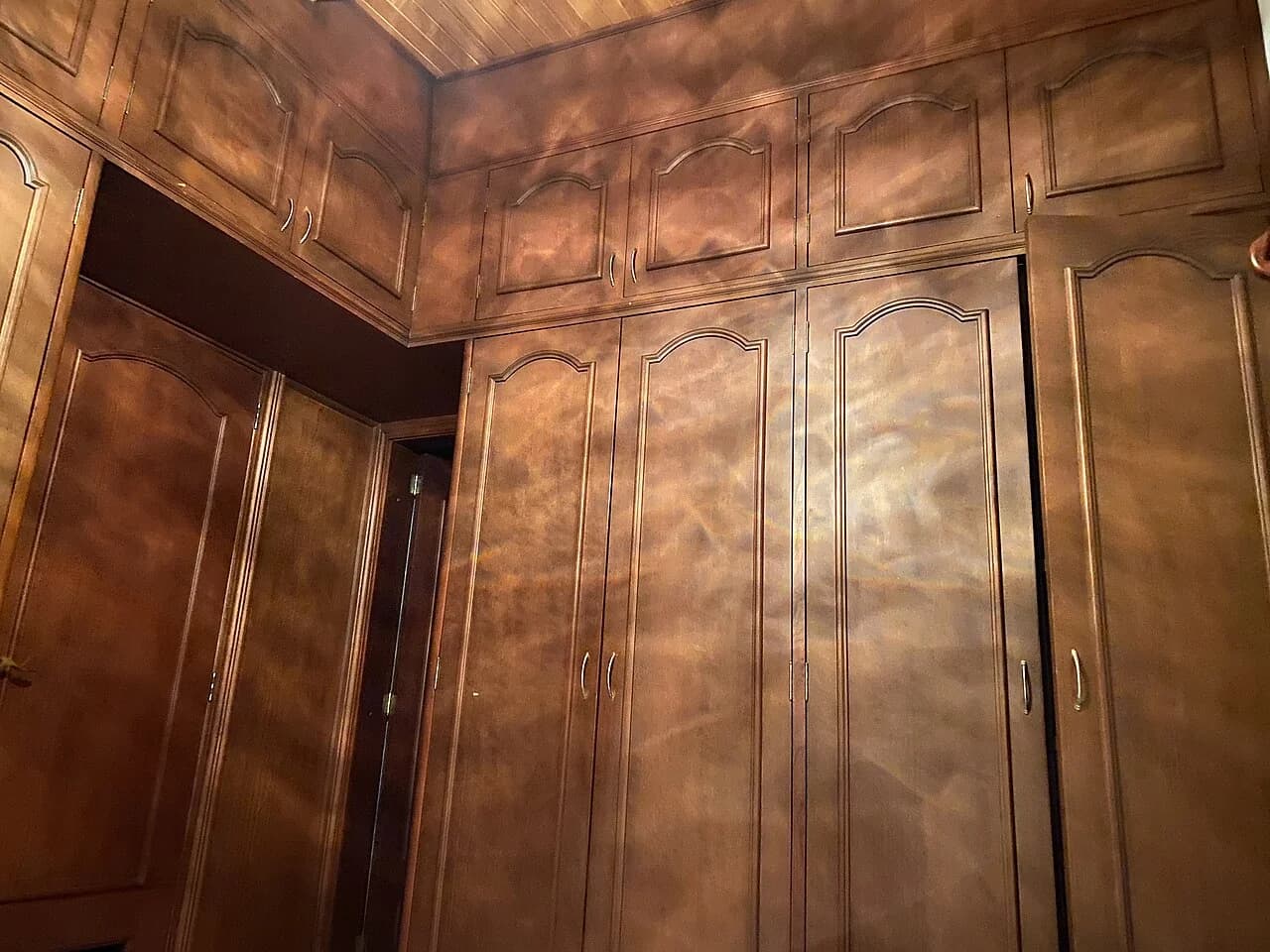 Floor-to-ceiling wooden built-in wardrobe with upper cabinets around a doorway