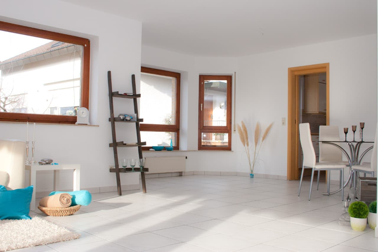Bright staged living room with white tile floor, three windows, a ladder shelf and a dining table