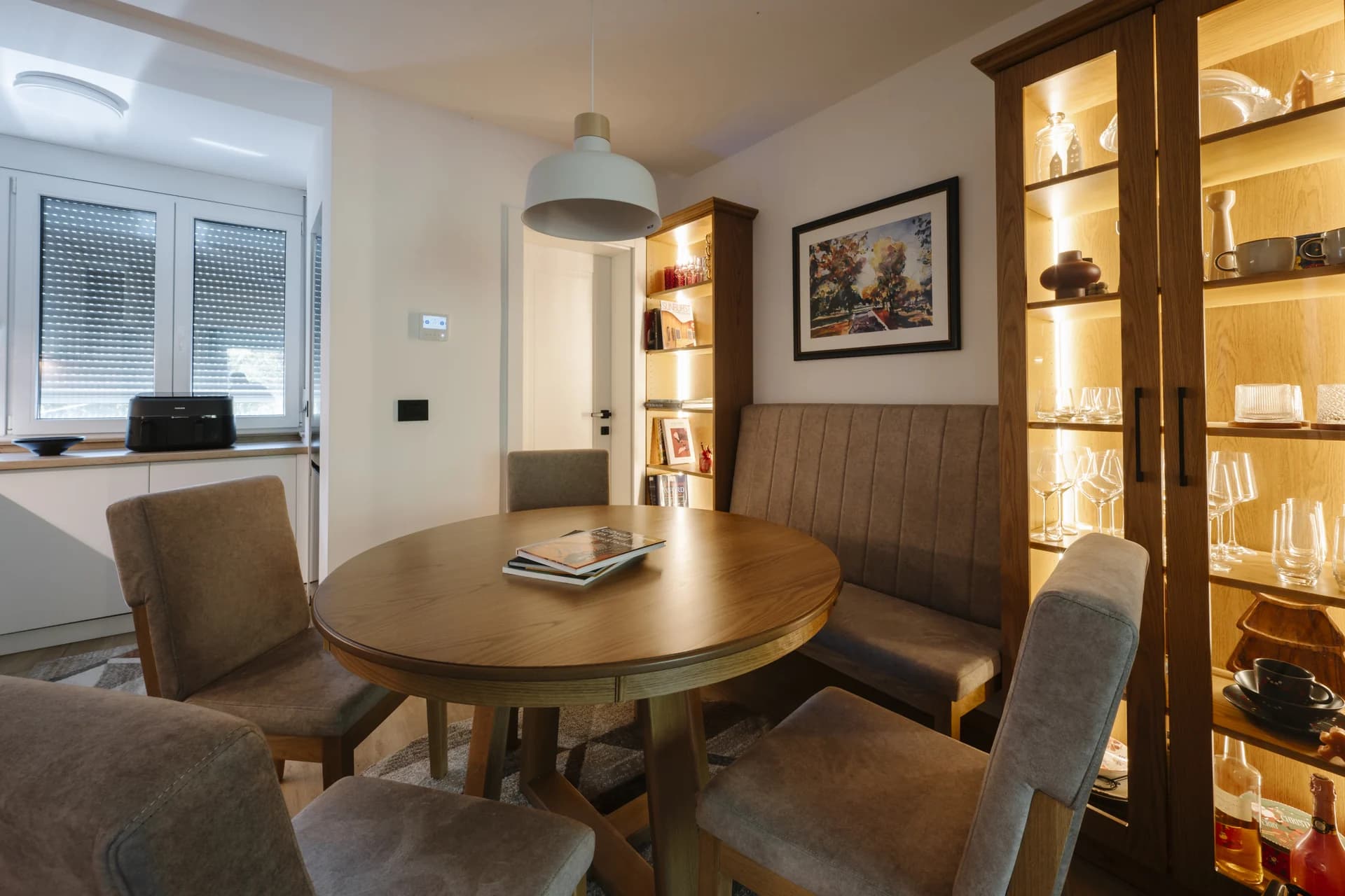 Wooden dining table with four chairs in a bright dining area beside a glass-front display cabinet
